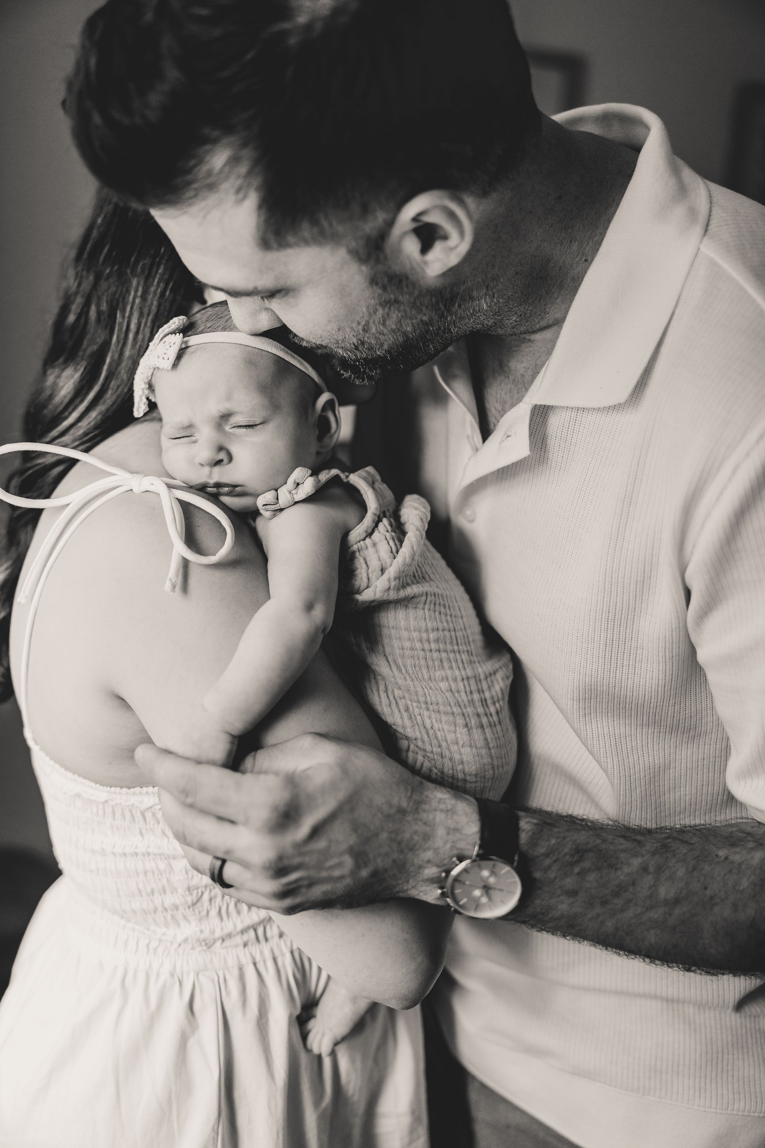A tender black and white photo series showing intimate moments between two parents and their newborn in white clothing.