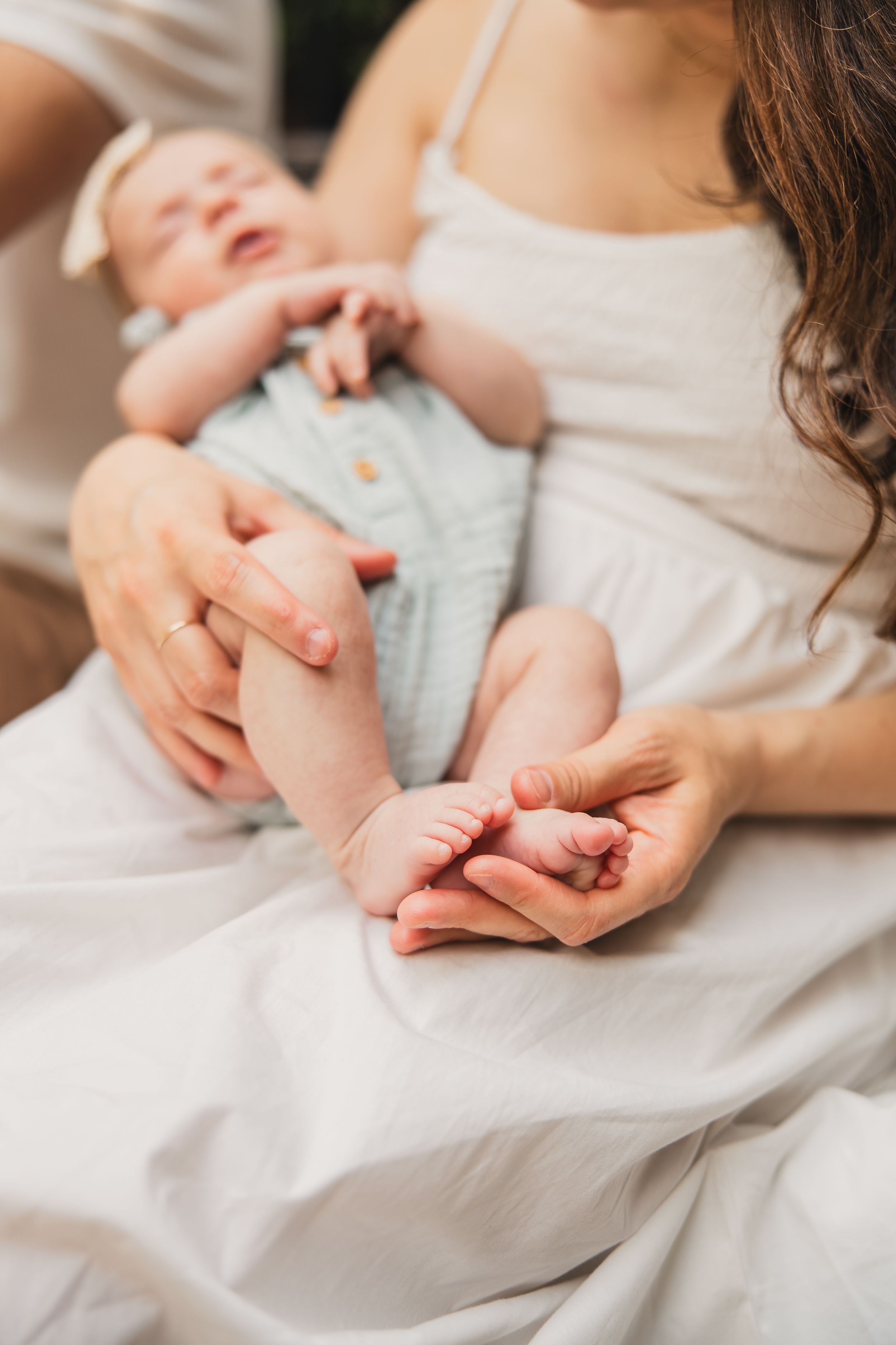 A tender moment showing tiny newborn feet being gently held in adult hands against white fabric.