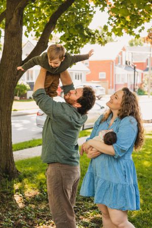 A family plays together on a grassy lawn with trees and buildings in the background.