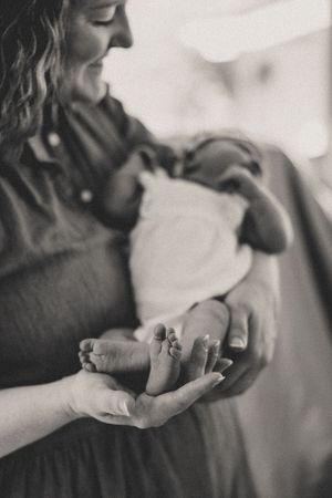 A tender black and white portrait of a mother holding her newborn baby's tiny foot in her hand.