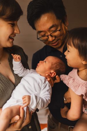 A series of intimate family moments captured in warm tones showing parents playing with their young child and newborn baby.