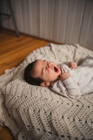 A sleepy yawning baby lies on a cozy knit blanket in a series of lifestyle photos.
