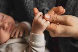 Close-up image showing tiny newborn hands holding their mother's finger.
