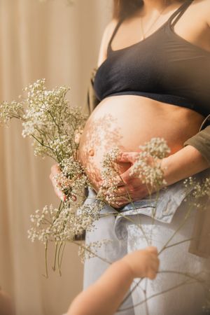 A pregnant woman in black top holds delicate baby's breath flowers against her belly in a soft, warm-lit maternity photo series.