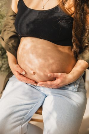 Close-up of a pregnant belly shown in multiple photos wearing a black top and jeans while a floral silhouette shines across it.