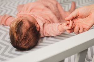 Baby wearing pink sleeper lies on gray and white chevron changing pad holding mom's hand.