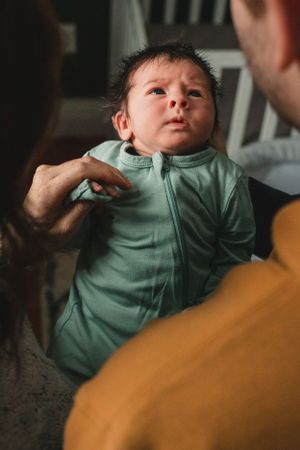 A baby wearing a mint green onesie is being held and makes various expressions in a sequence of photos.
