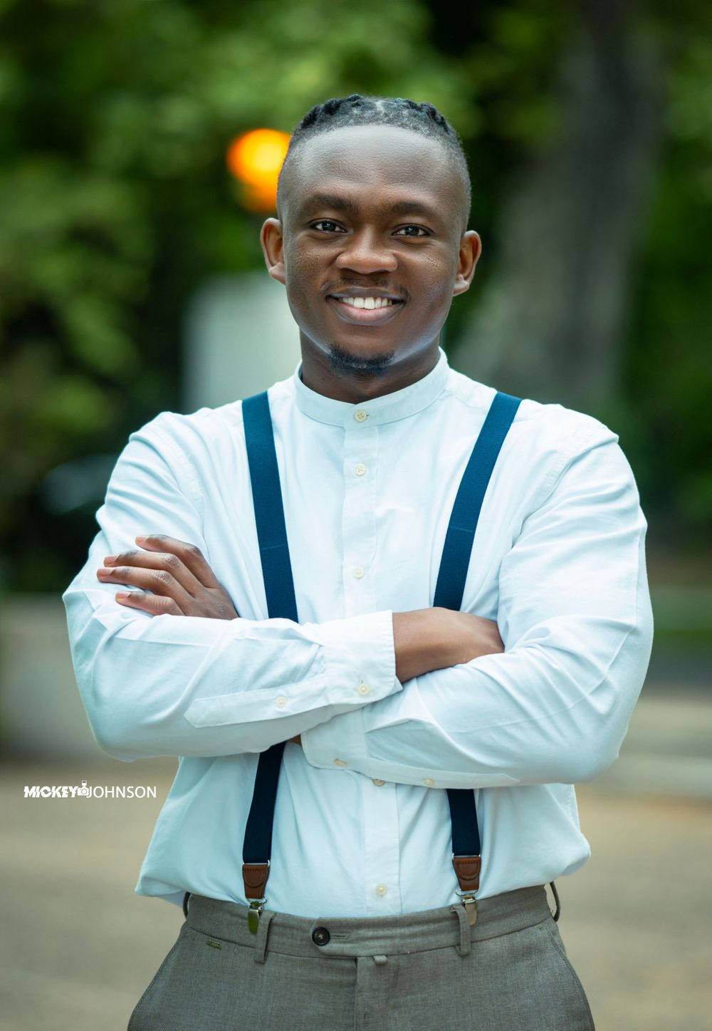 Professional portrait of person in white shirt and navy suspenders outdoors.
