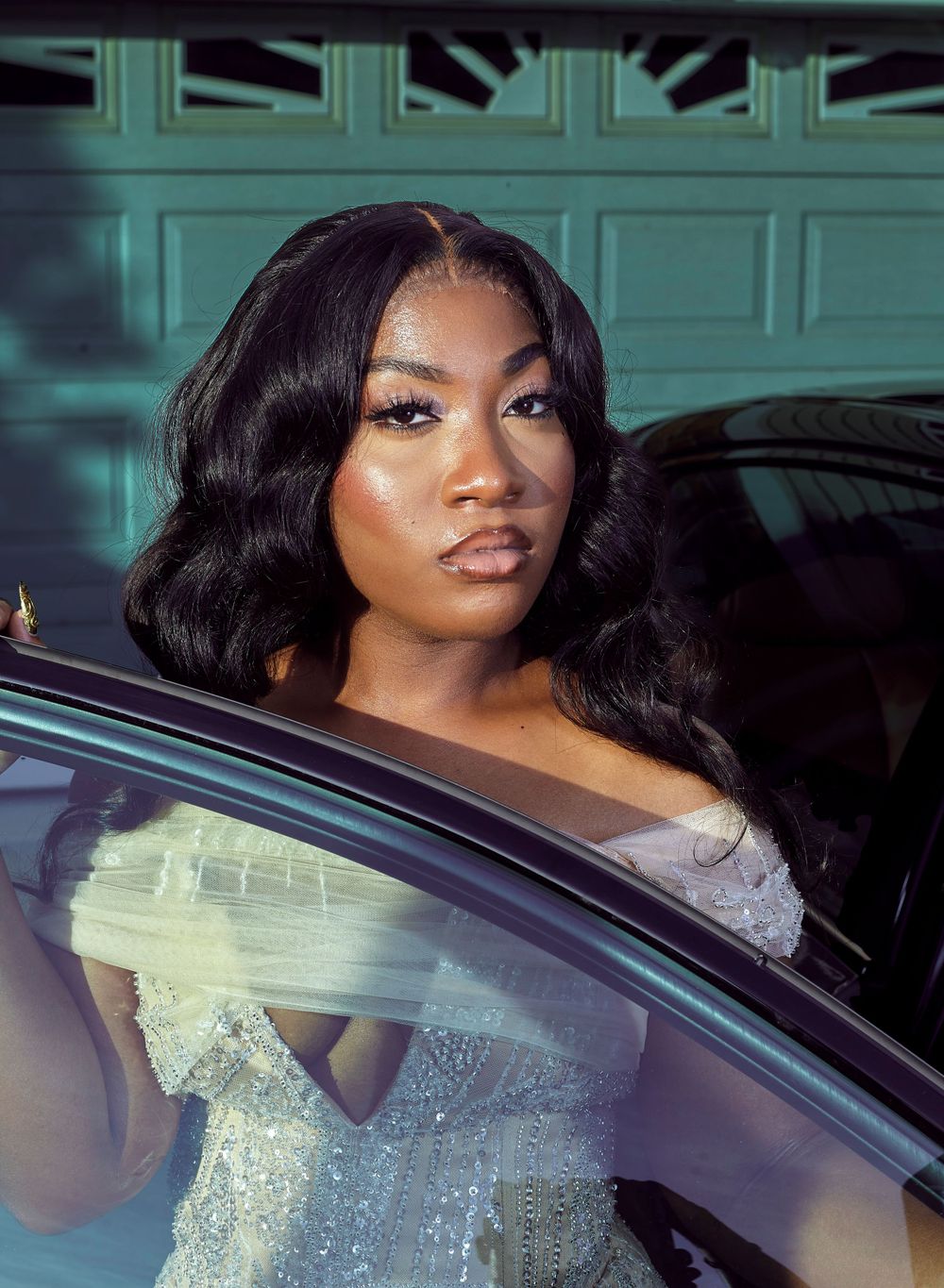 A sparkling silver sequined dress is shown through a car window in an elegant photoshoot setting.