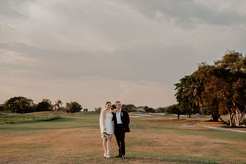 A couple stands together on a scenic golf course at sunset with oak trees in the background.