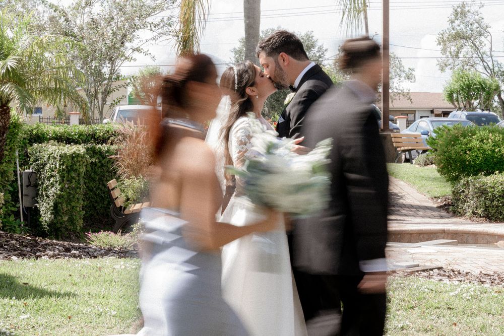 A couple in formal wedding attire dances together in a garden setting during a celebration.