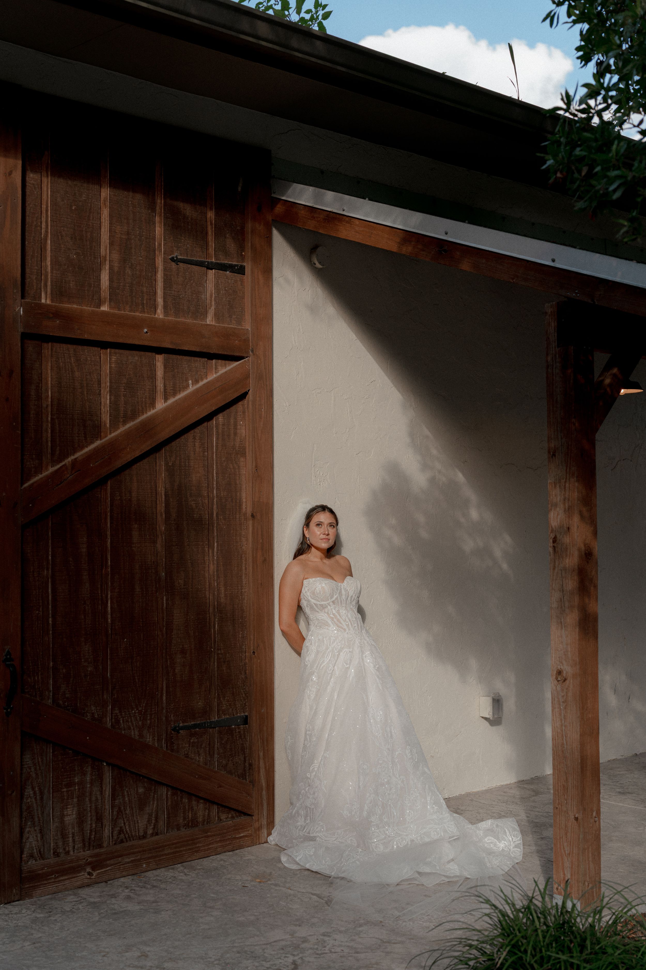 A flowing white wedding dress photographed in a rustic wooden doorway setting with dramatic lighting.
