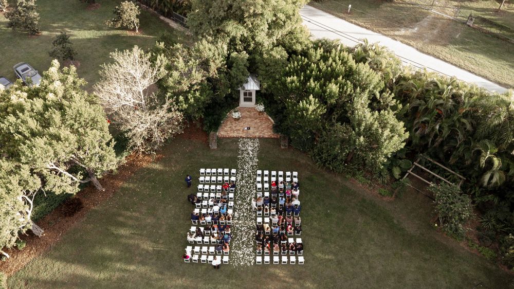 Aerial view of an outdoor wedding ceremony with white chairs arranged in rows on a lush green lawn.
