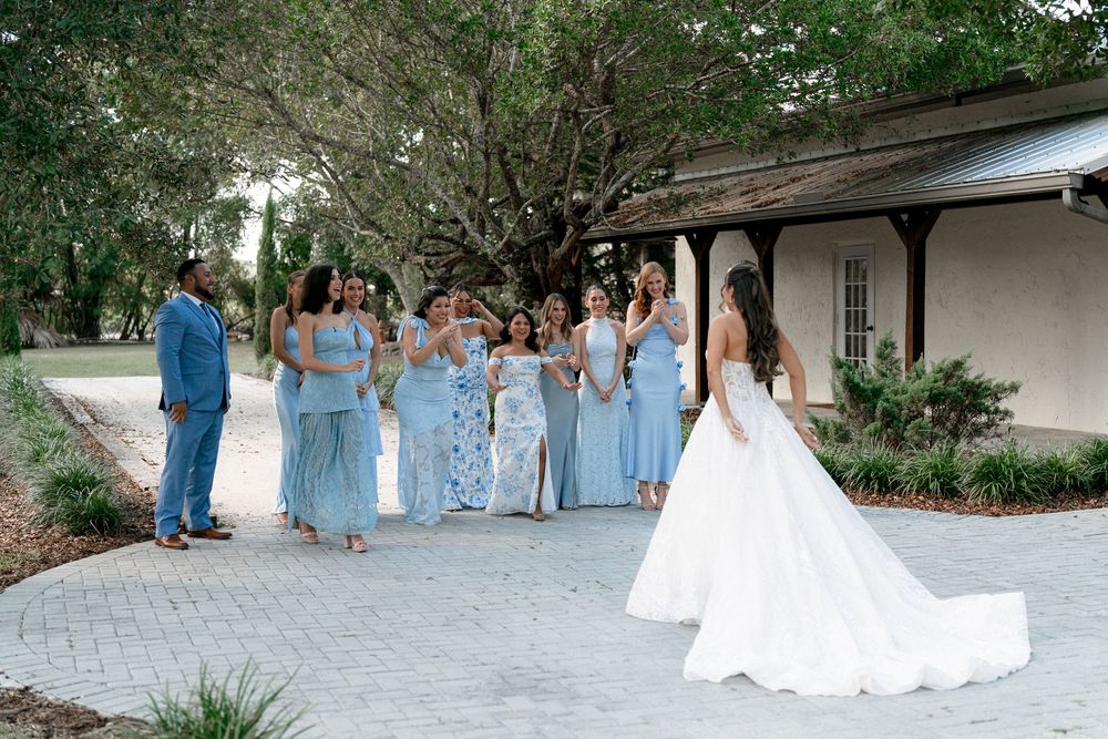 Wedding party in light blue dresses walking outdoors along a garden pathway during a sunny day.