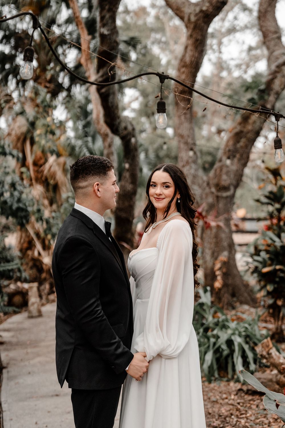 A romantic couple shares tender moments in a wooded setting with eucalyptus trees creating a dreamy atmosphere.