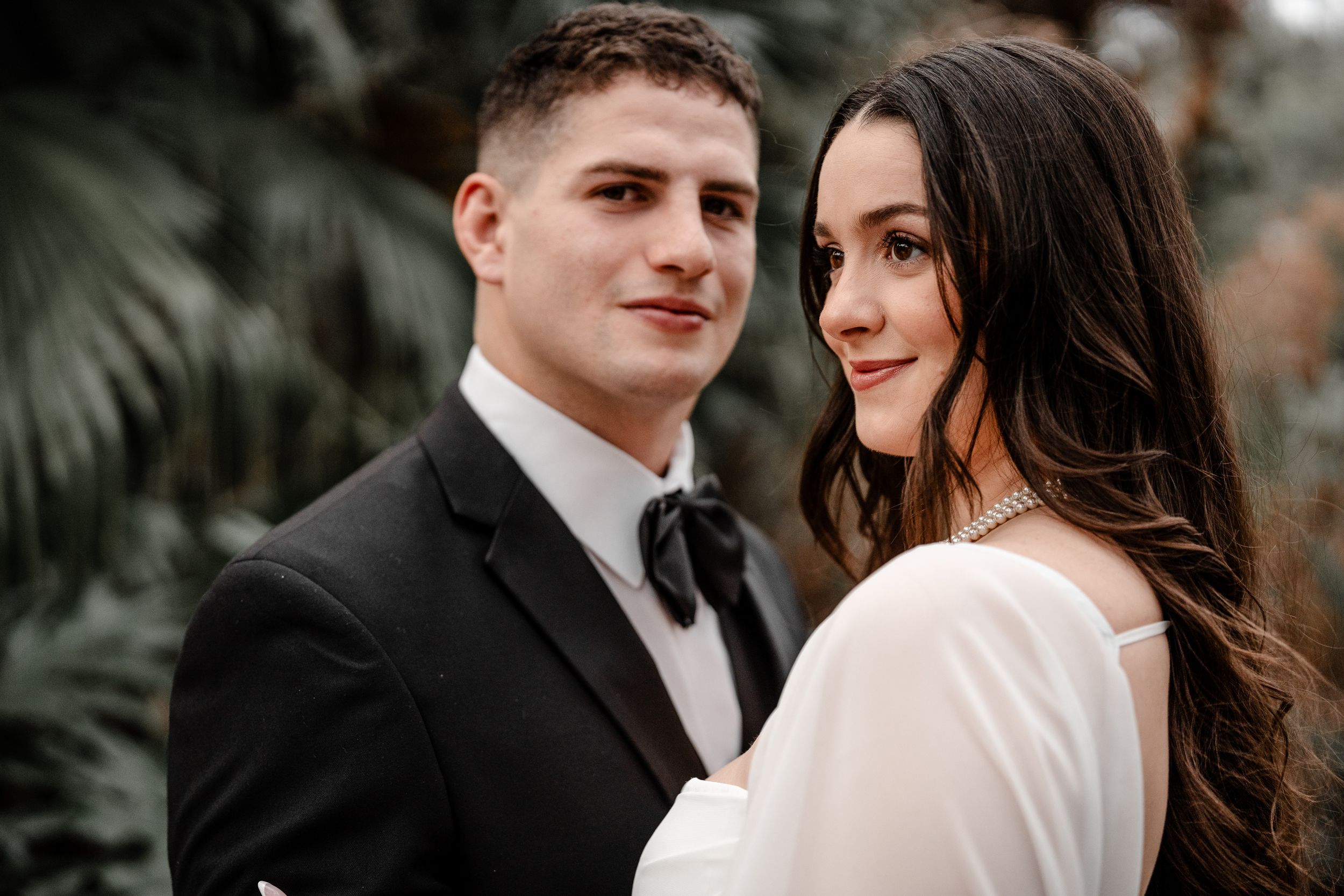 A couple in formal wedding attire poses intimately together during an outdoor photo session.