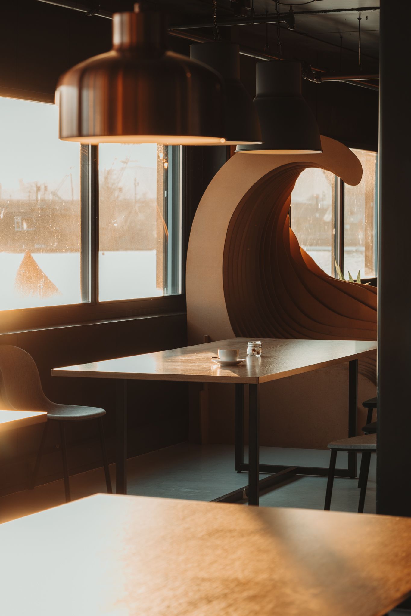 Modern restaurant interior with curved booth seating and tables illuminated by warm natural light through windows.