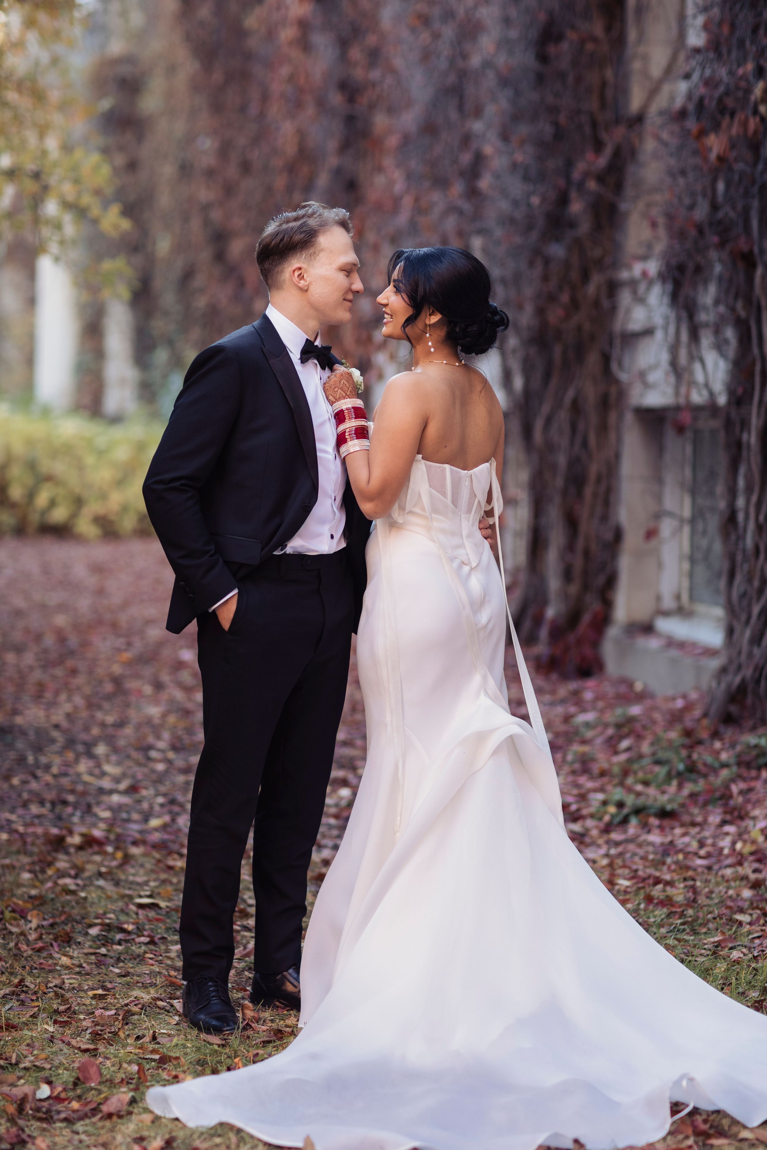 Bride and groom share a romantic moment outdoors, surrounded by autumn foliage, in elegant wedding attire.