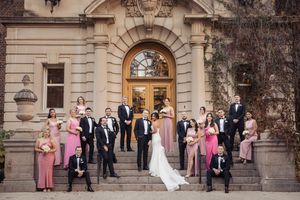 Wedding party poses outside elegant stone building with arched doorways and classic architecture.