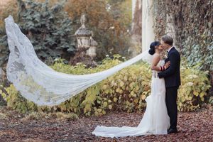 A flowing white wedding veil catches the breeze in an autumn garden setting during a romantic moment.