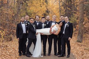 Wedding party poses together on fallen autumn leaves in a forest setting during golden hour.