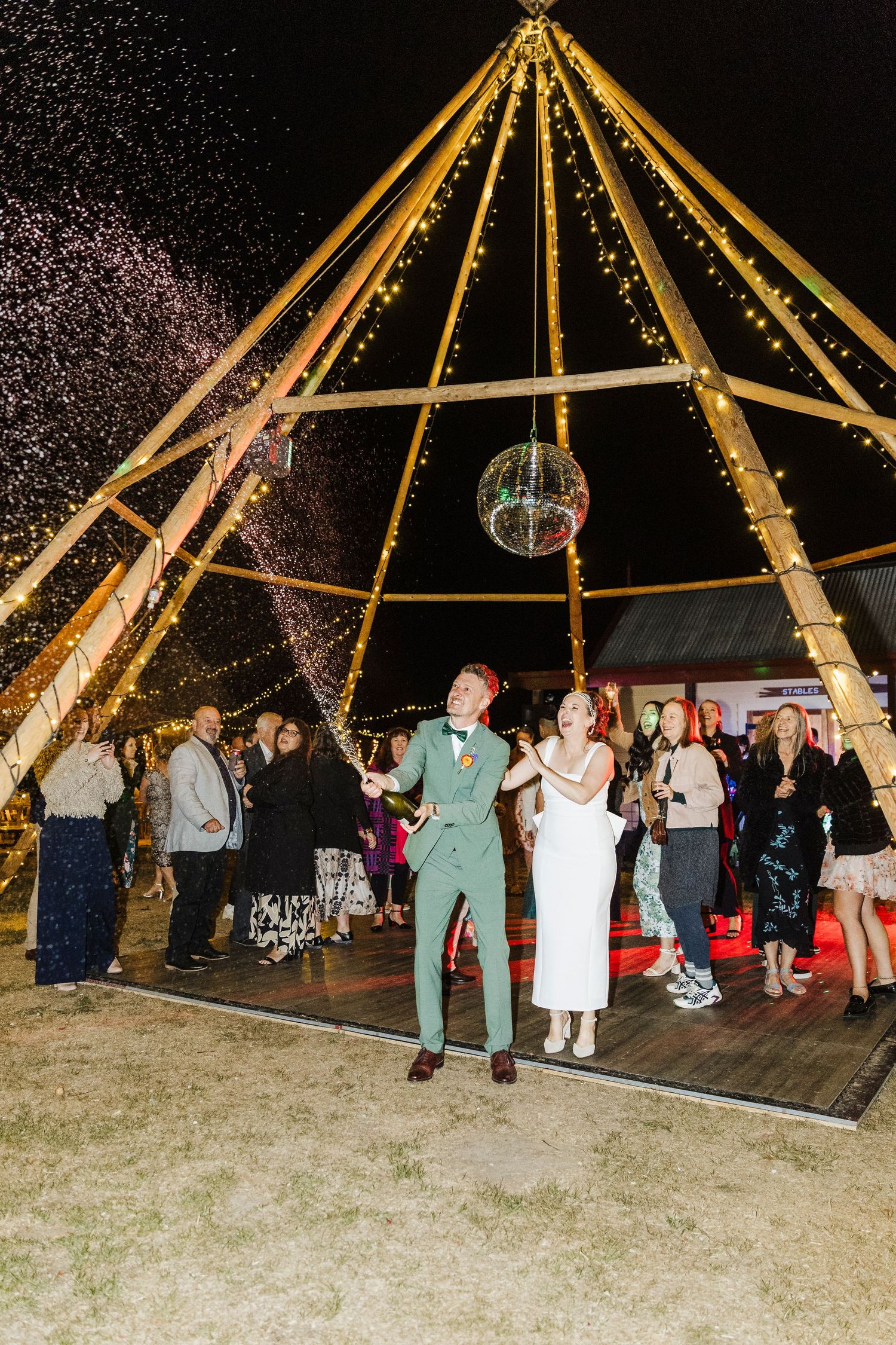 Wedding reception under illuminated tent structure with disco ball and dancing.