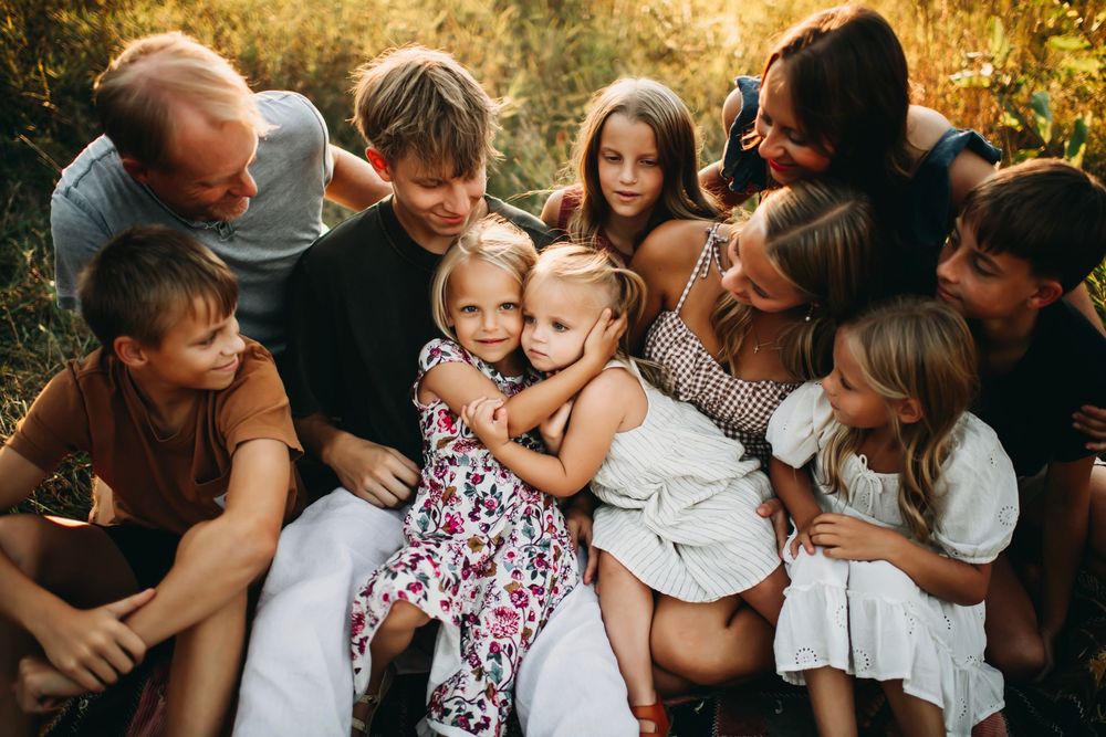 Large family group hugging together outdoors in golden sunlight, children and adults sharing a warm embrace in a natural setting.
