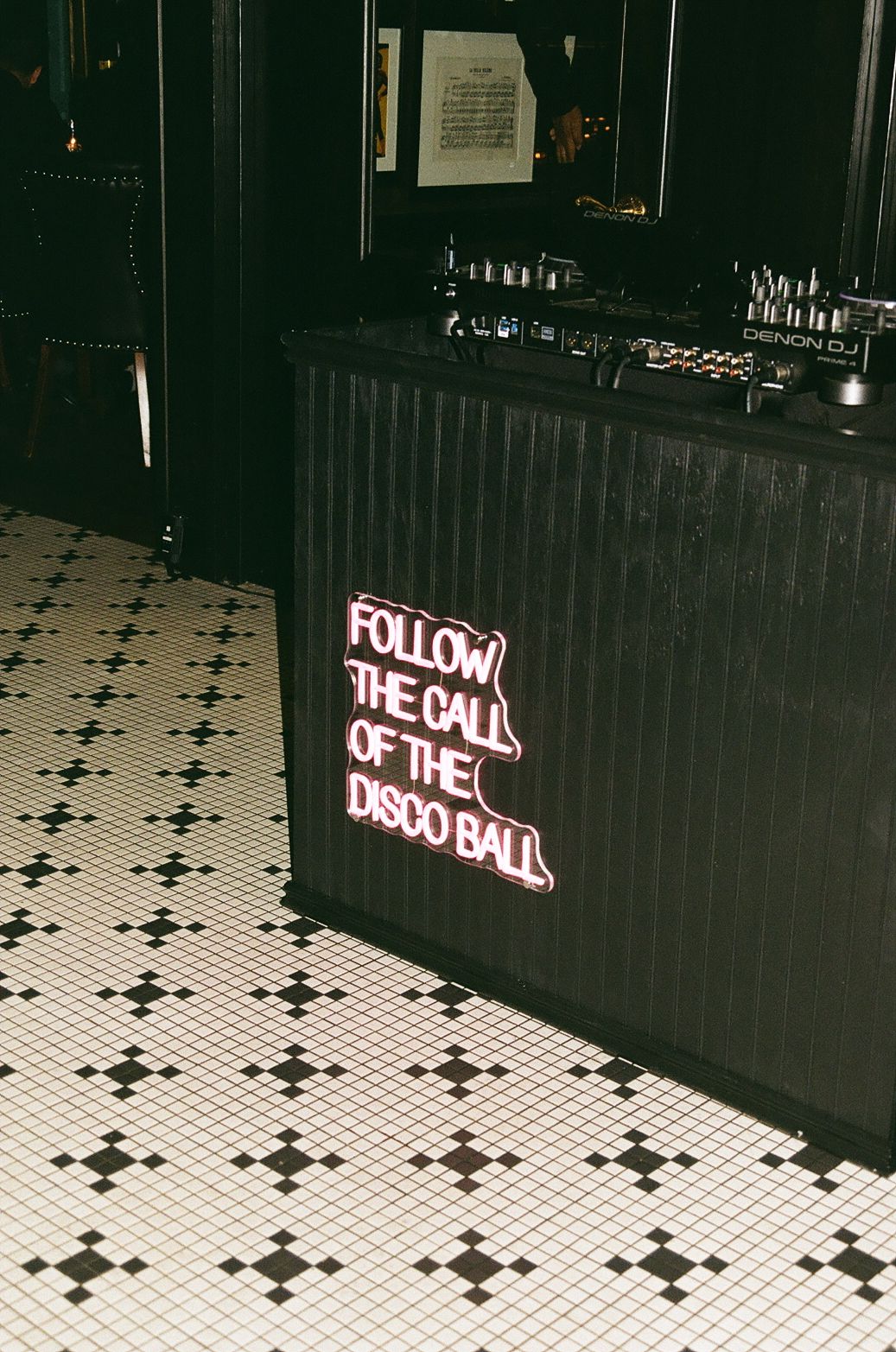 Neon sign reading 'Follow the Call of the Disco Ball' above checkerboard floor tiles.