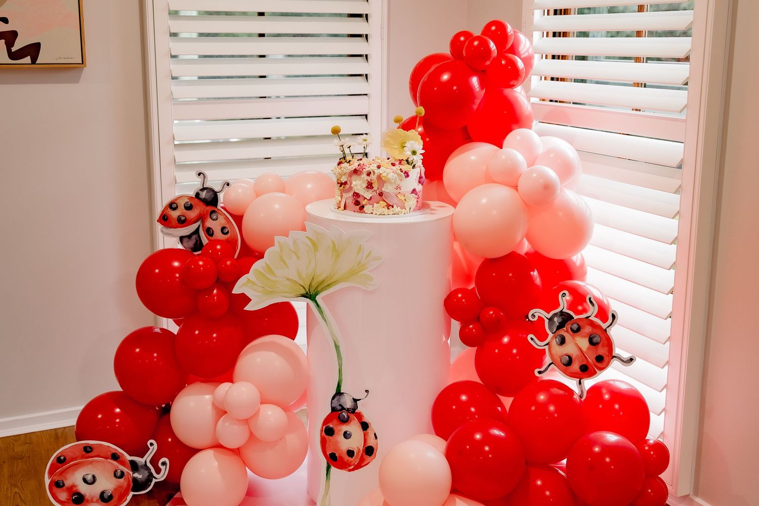 Whimsical balloon arch with red and pink balloons featuring ladybug decorations.