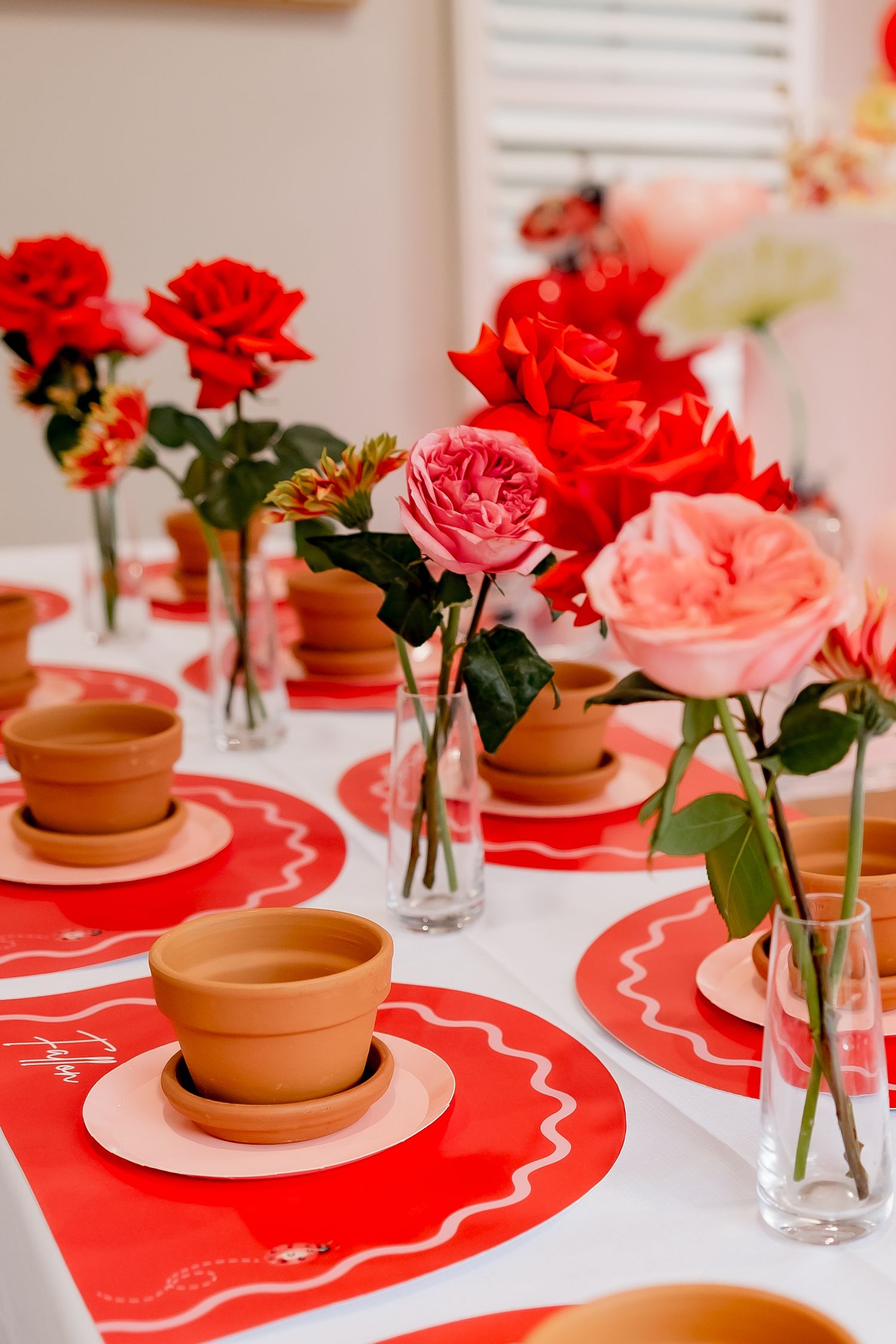 Elegant table setting with red and pink roses in vases alongside terracotta pots.
