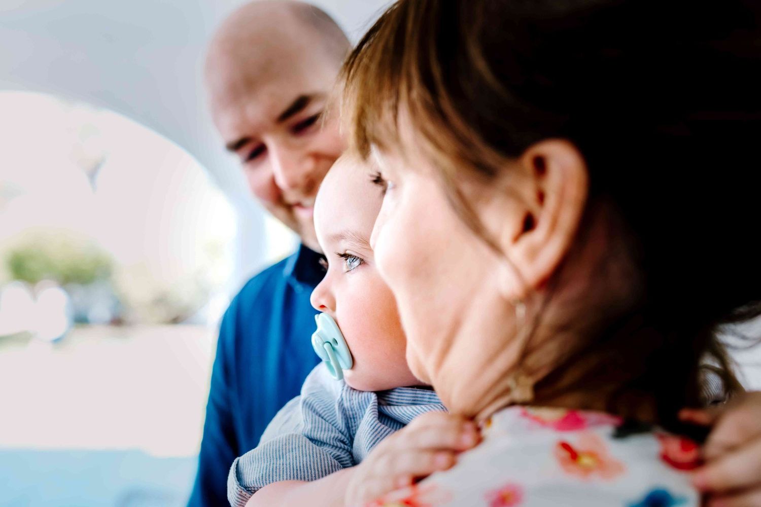 Father and mother hold their baby between them, both looking towards the light.