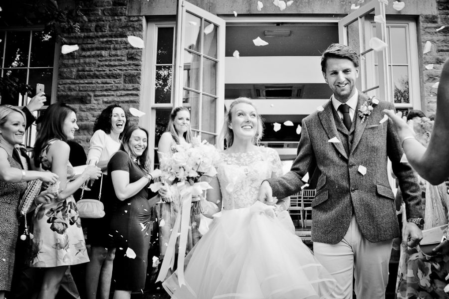 Wedding couple exits building while guests blow bubbles and celebrate.