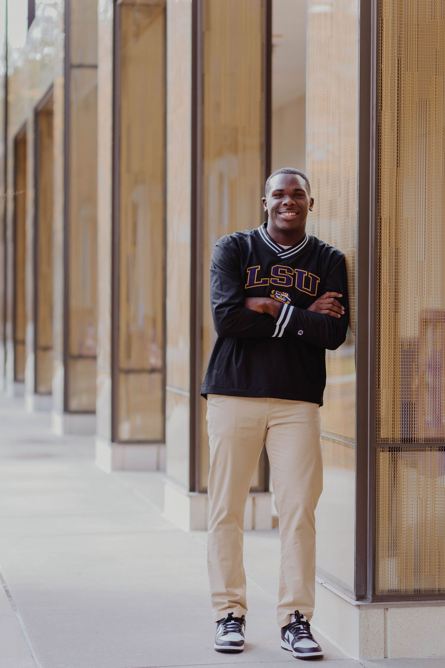 Student in LSU sweatshirt smiles while standing against campus building columns.