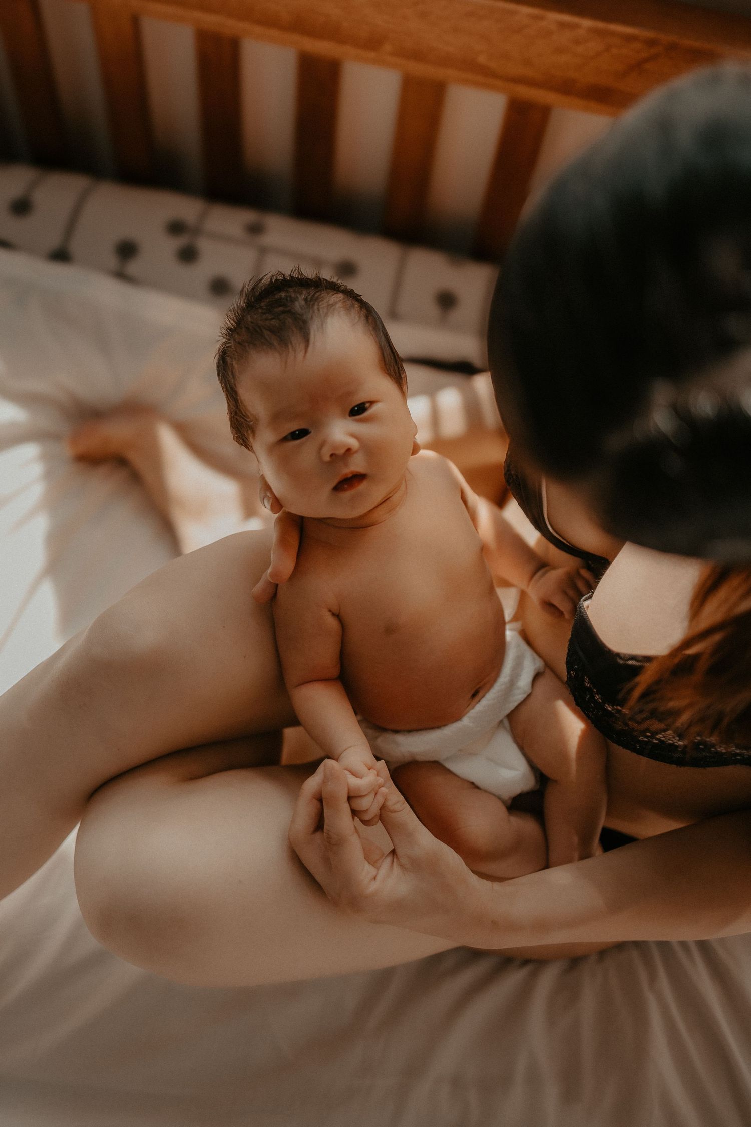 Candid moment of parent and infant bonding on a cozy bed in warm natural lighting.