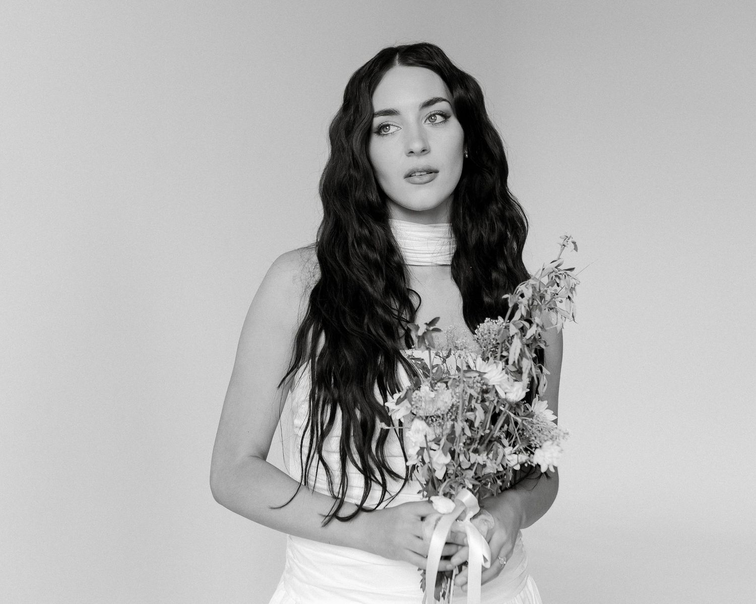 A black and white portrait showing a person in white holding a delicate floral bouquet.