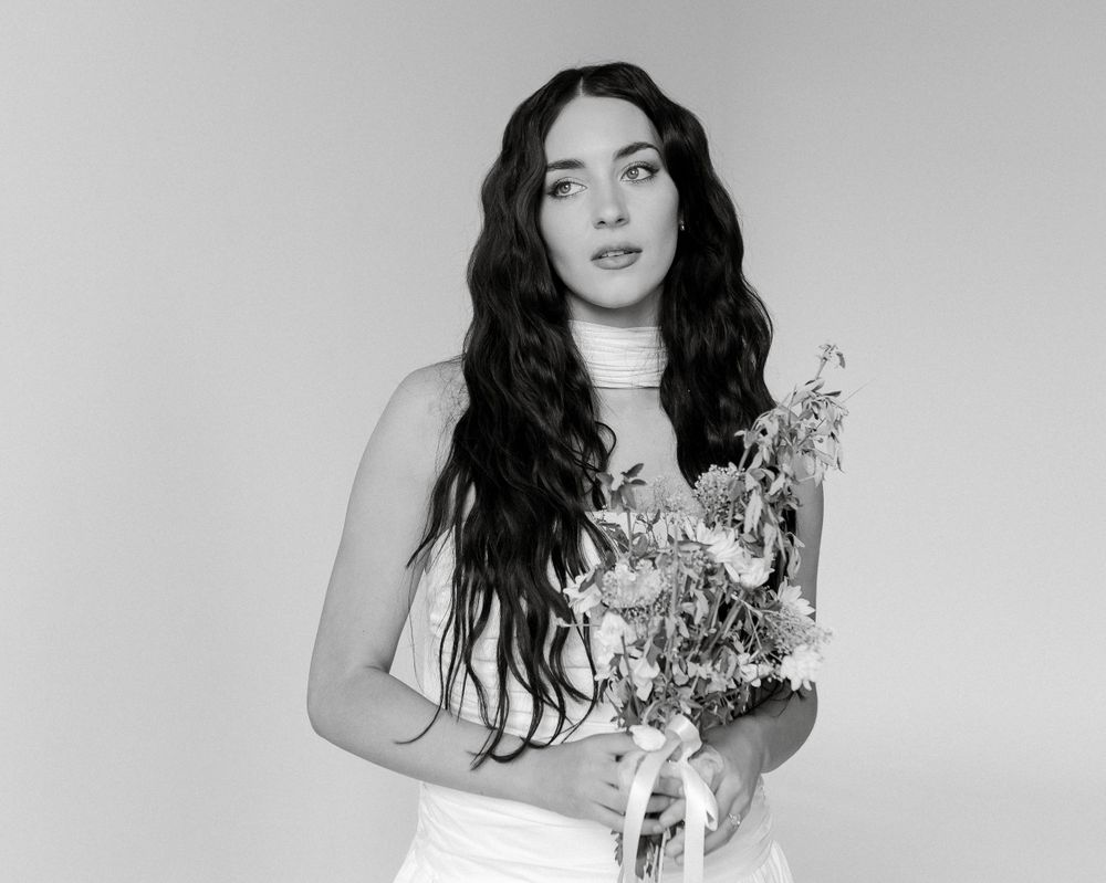 A black and white portrait showing a person in white holding a delicate floral bouquet.