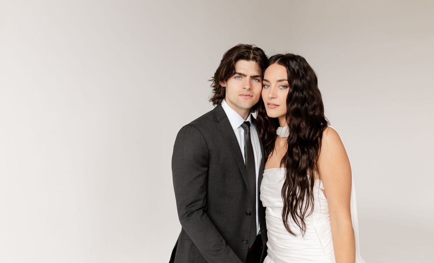 A romantic studio portrait of a couple in formal attire against a white background.