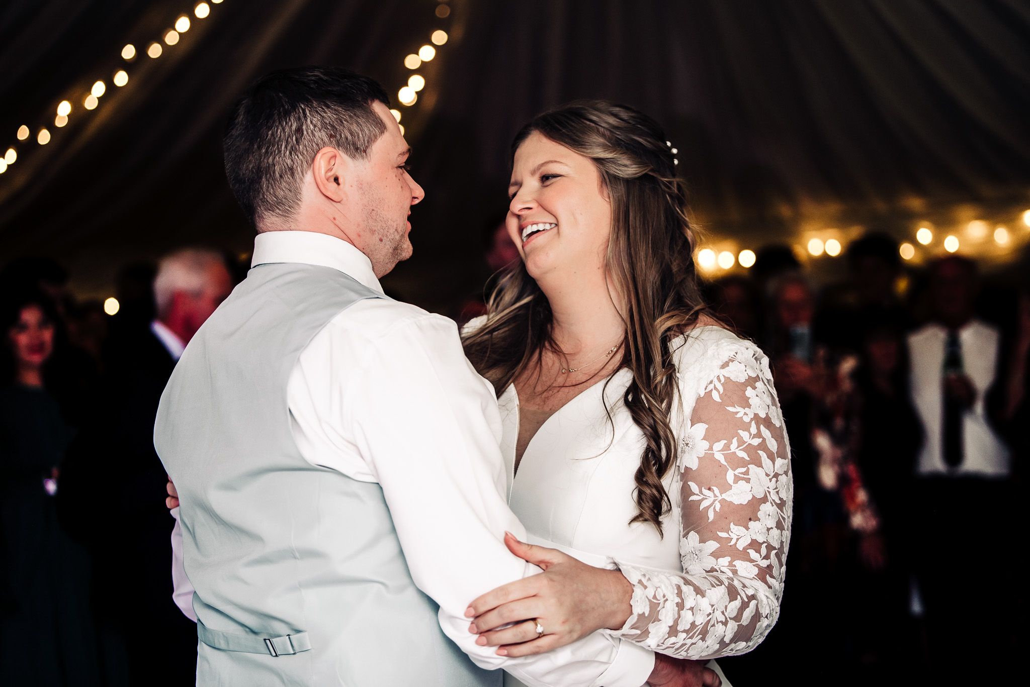 Wedding couple dancing under string lights in romantic evening reception setting.