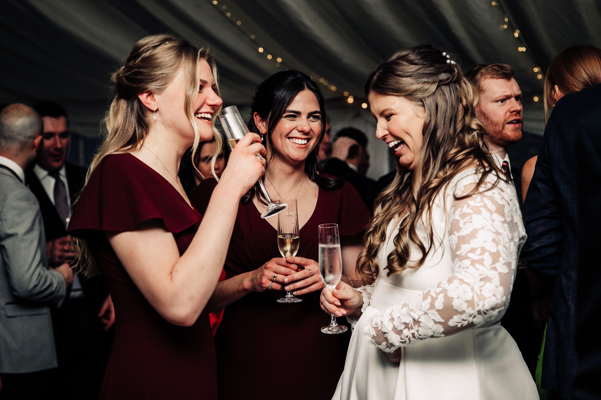Wedding party enjoying drinks and laughter during evening reception.
