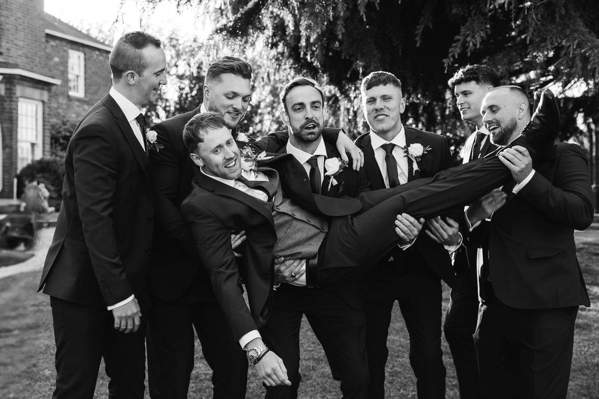 Groomsmen in black suits laughing together during wedding celebration.