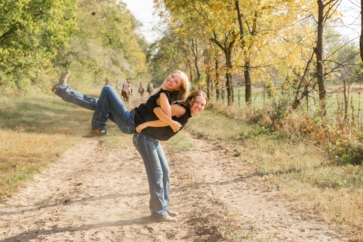 Best friends dancing on a dirt path surrounded by autumn trees.