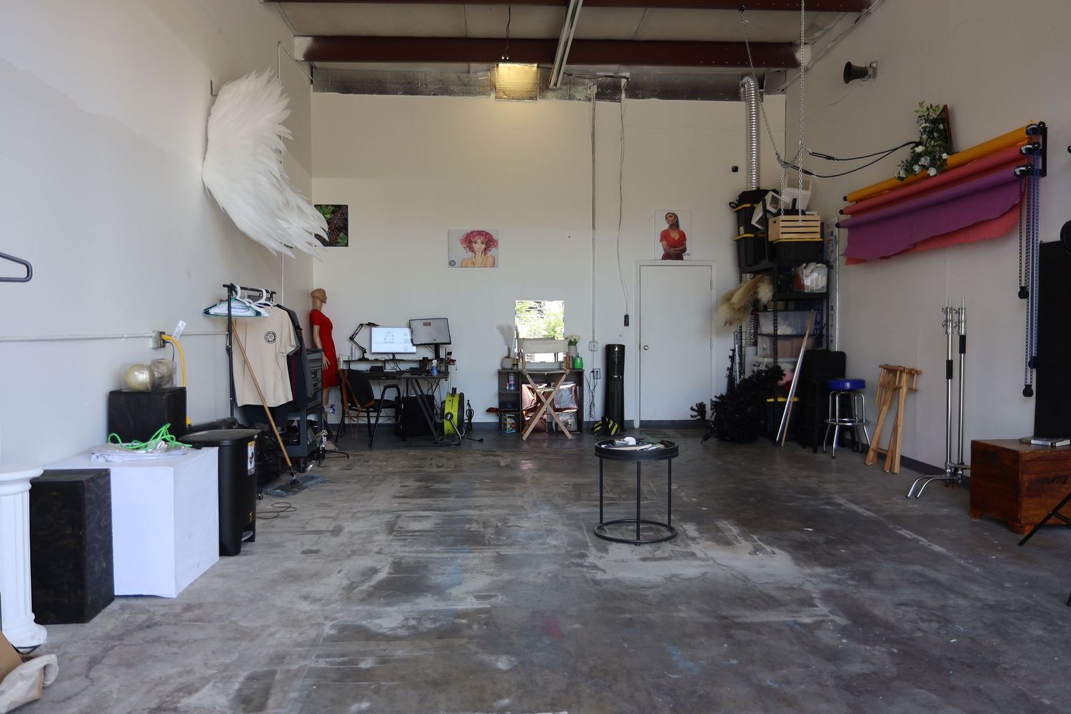 Interior view of a garage converted into a workspace with concrete floors, exposed beams, and scattered equipment.