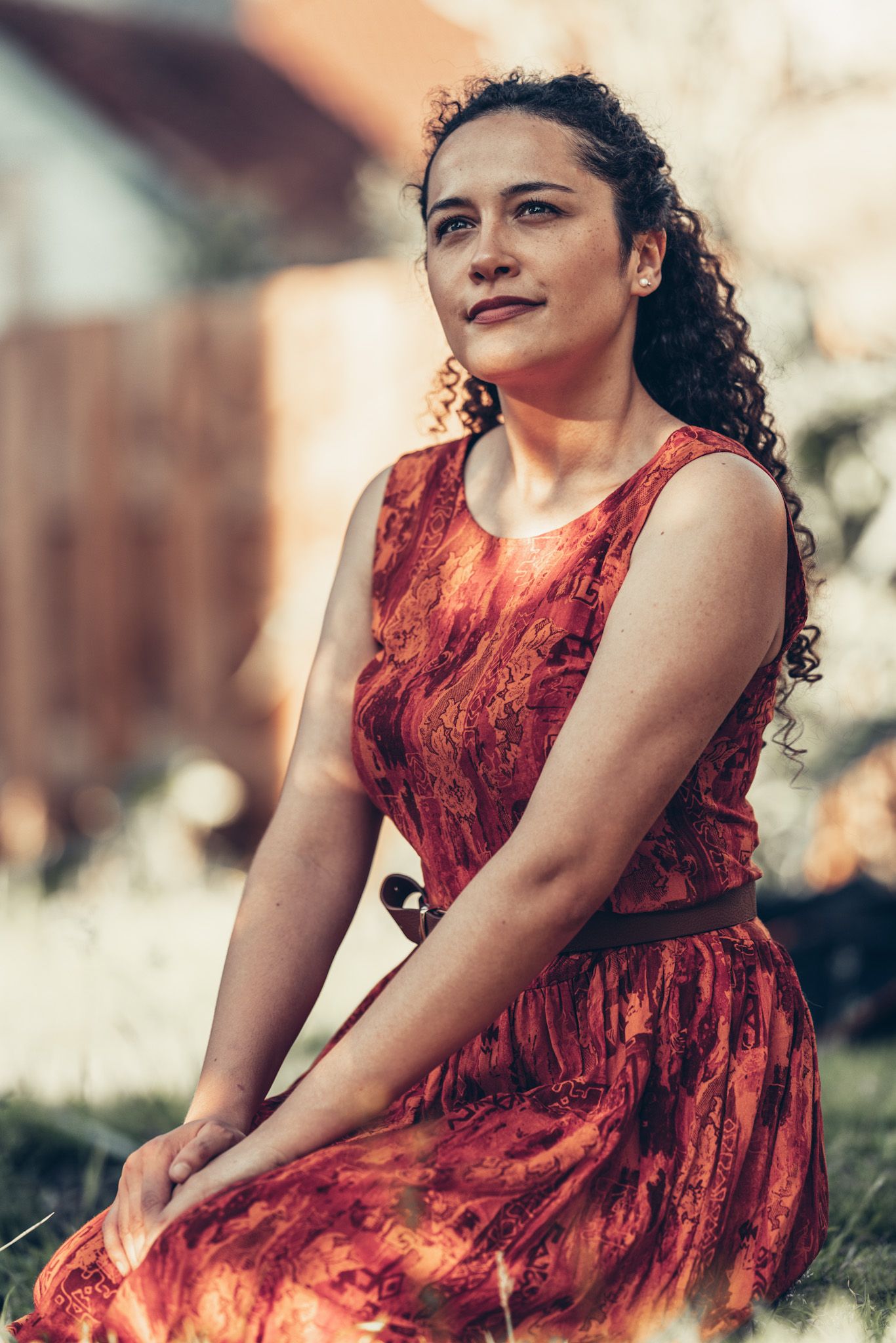 A person in a burgundy lace dress poses gracefully outdoors in a dreamy, natural setting.