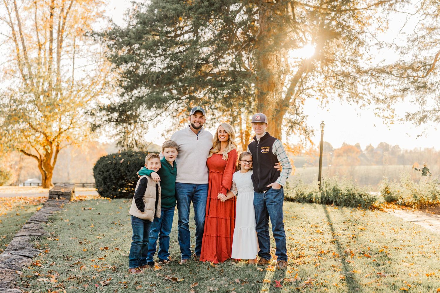 Outdoor family autumn portrait with sunlight filtering through colorful trees.
