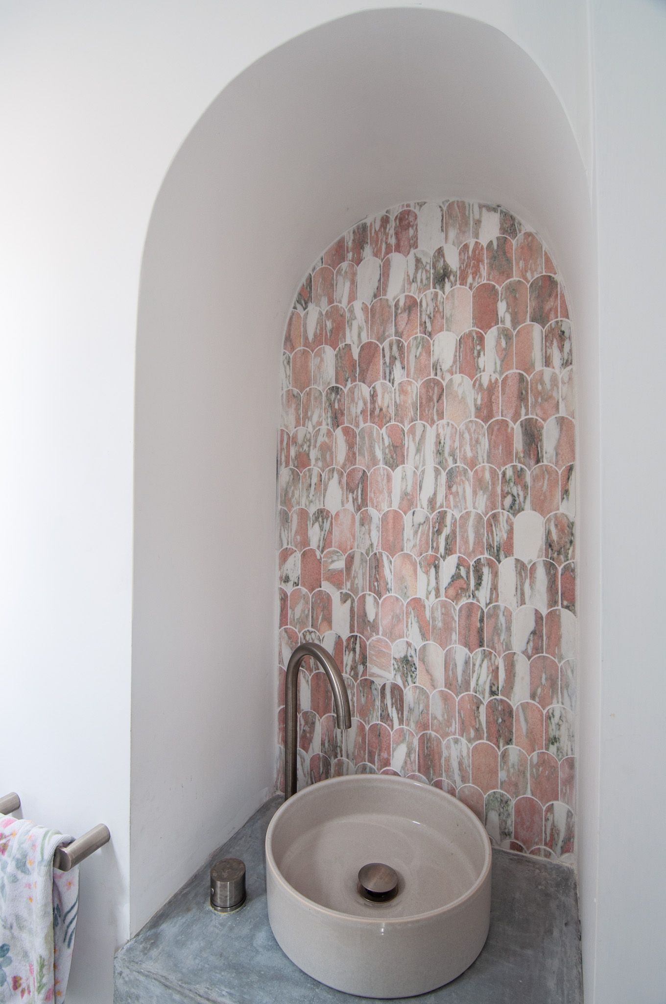 Arched alcove sink area with pink patterned tile backdrop and modern round vessel basin.