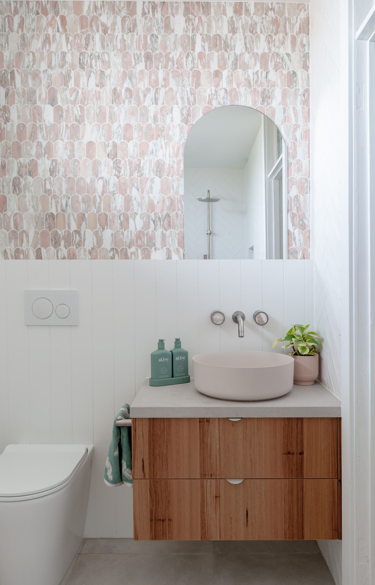 Modern bathroom with pink patterned wallpaper, floating wooden vanity, and round vessel sink.