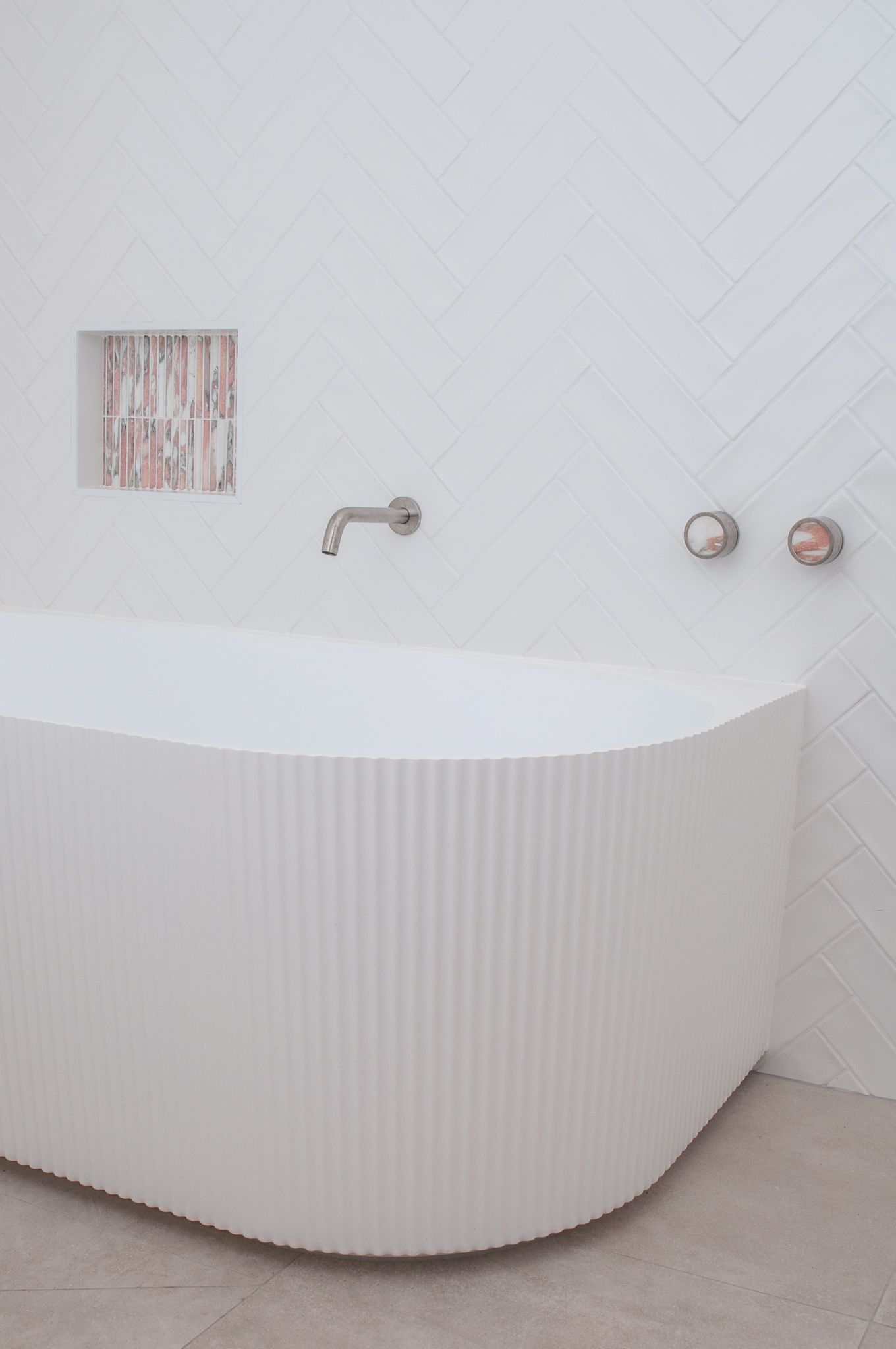 Minimalist bathroom featuring a ribbed freestanding tub with wall-mounted fixtures against white tile.