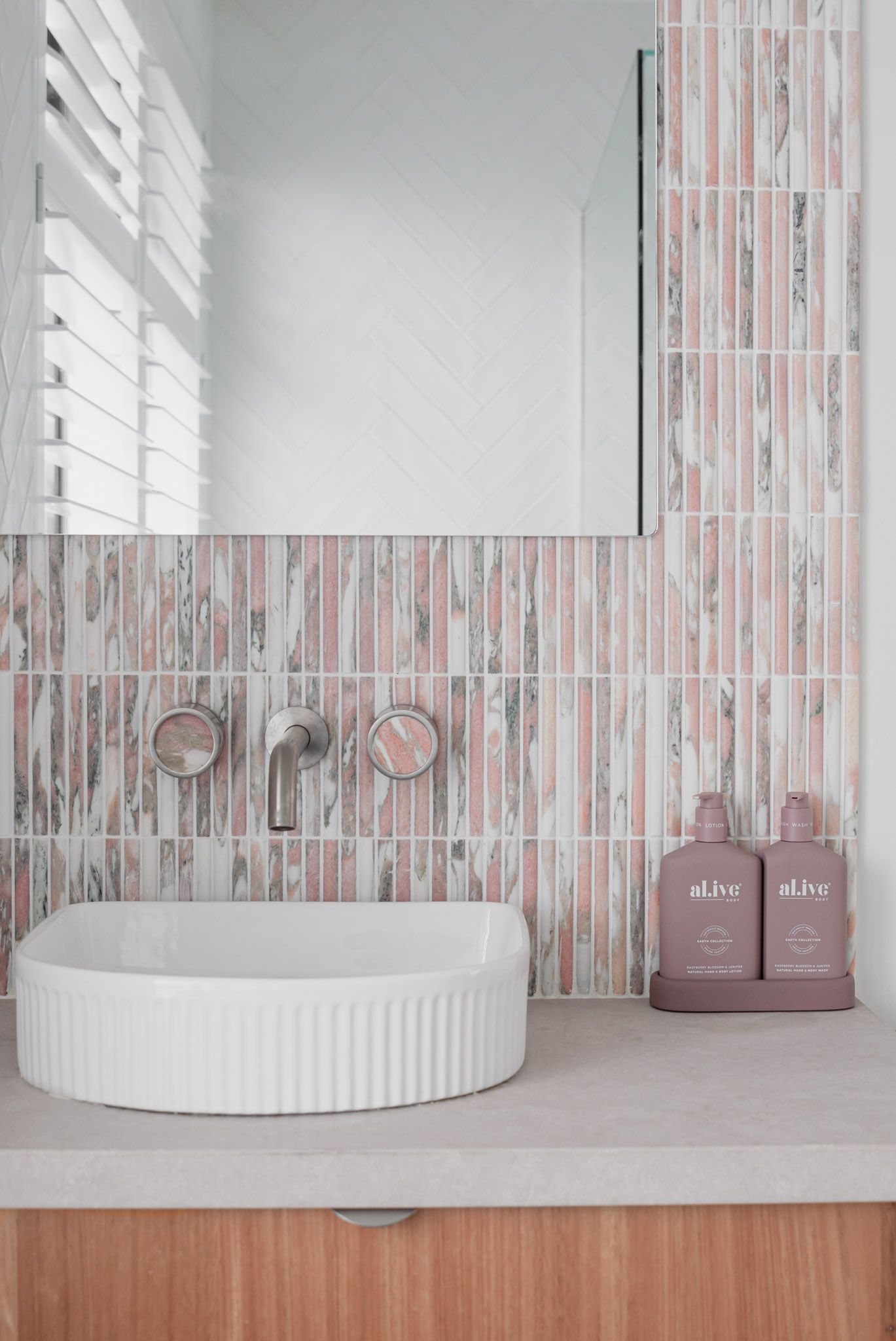 Contemporary bathroom vanity with striped pink tile backsplash and white vessel sink.