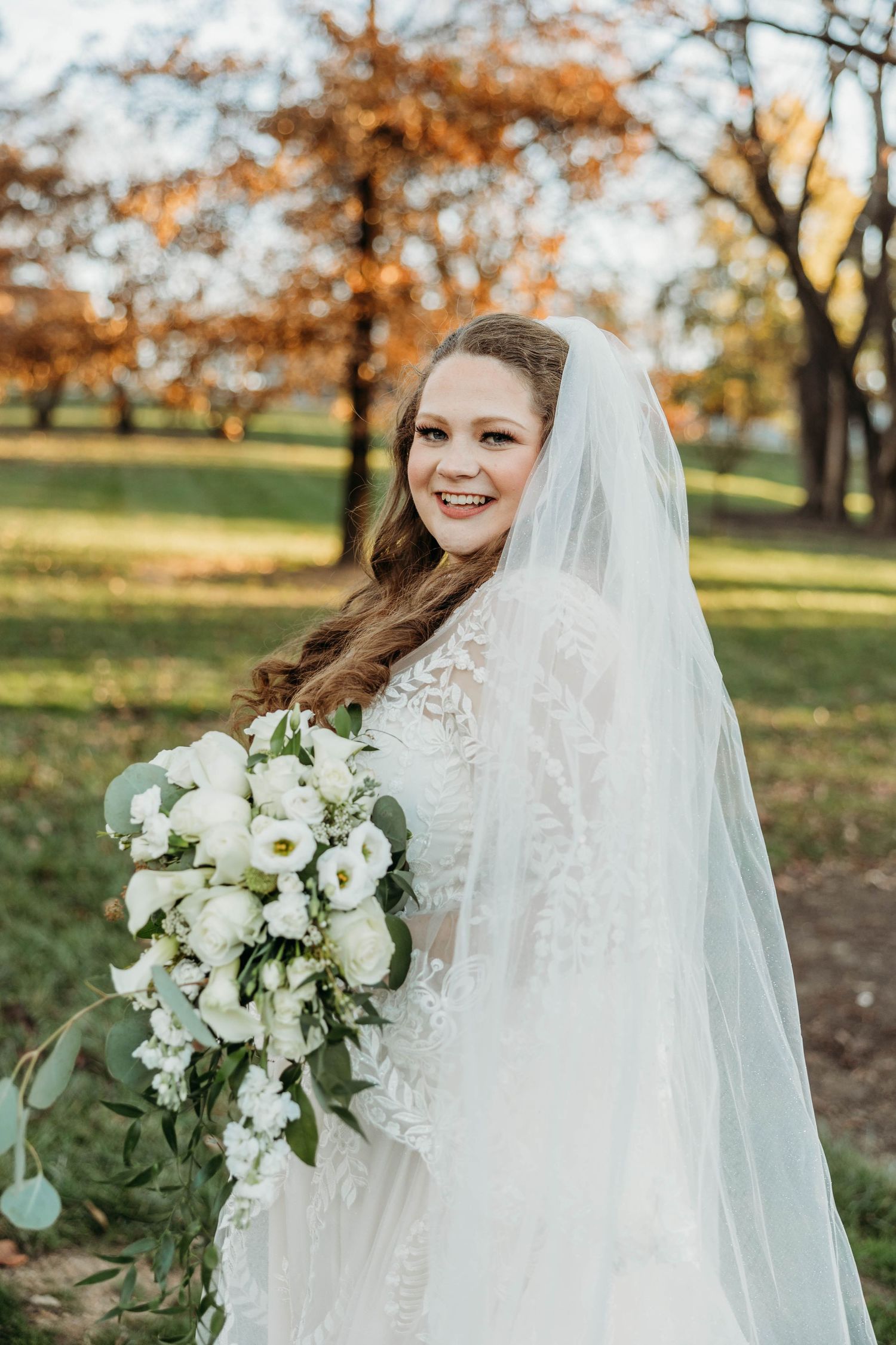 Beautiful bridal portrait in a fall setting with a flowing veil and white floral bouquet.