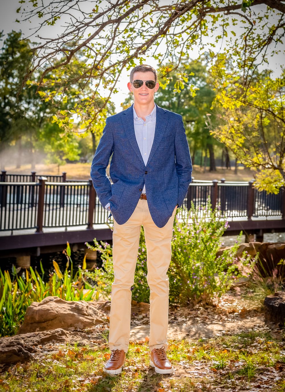 A teenager in navy blazer and khakis poses confidently by ornate bridge railing.